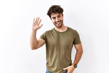 Hispanic man standing over isolated white background waiving saying hello happy and smiling, friendly welcome gesture 
