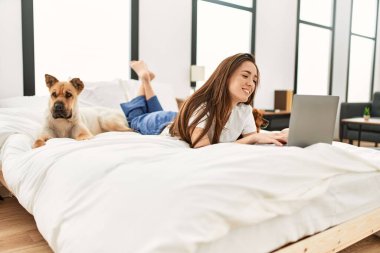 Genç İspanyol kadın yatak odasında köpeklerle birlikte dizüstü bilgisayar kullanıyor.
