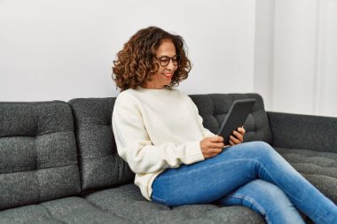 Orta yaşlı İspanyol kadın evde dokunmatik ped kullanarak gülümsüyor.