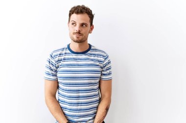 Yakışıklı genç adam izole edilmiş arka planda duruyor. Gülümsüyor, yan tarafa bakıyor ve düşünüyor.. 