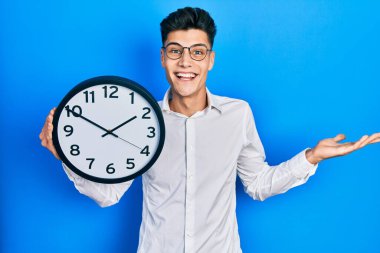 Genç İspanyol adam büyük bir saat tutuyor başarıyı mutlu bir gülümsemeyle ve kazanan yüz ifadesiyle kutluyor. 