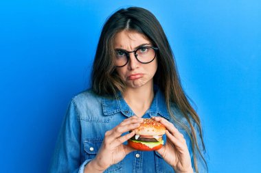 Lezzetli klasik bir burger yiyen beyaz bir kadın bunalımda ve üzüntüden ağlıyor, ağlıyor ve korkuyor. hüzünlü ifade. 