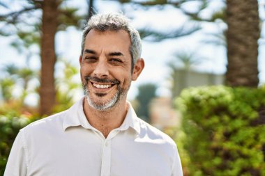 Orta yaşlı, kır saçlı, gülümseyen bir adam şehirde mutlu bir şekilde duruyor..