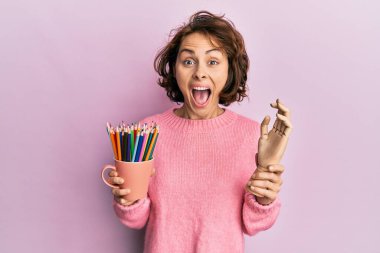 Genç esmer kadın küçük ahşap manikin elinde ve kalemlerle çılgınlığı kutluyor ve başarı için hayrete düşüyor.. 