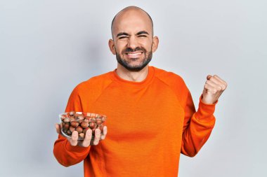 Çıplak fındık tutan genç kel adam gururla haykırıyor, zaferi kutluyor ve başarıyı kollarını kaldırarak kutluyor. 