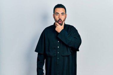 Sakallı, Katolik rahip cüppeli yakışıklı bir adam. İnançsızlıktan, şaşkınlıktan ve elleri çenesinde olan şaşkınlıktan büyülenmiş görünüyor. 