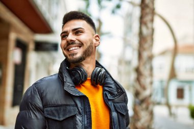 Sakallı yakışıklı, neşeli ve kendine güvenen, kışlık palto ve kulaklık takan bir İspanyol.