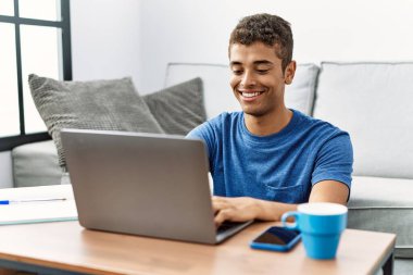 Genç İspanyol adam evde dizüstü bilgisayar kullanıyor.