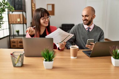Ofiste bilgisayar ve akıllı telefon kullanarak çalışırken gülümseyen iki İspanyol iş adamı..