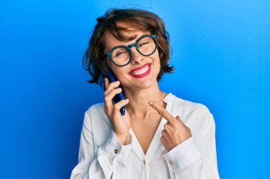 Genç esmer kadın akıllı telefondan konuşuyor. Gülümsüyor. Elinle ve parmağınla mutlu mesut işaret ediyor. 