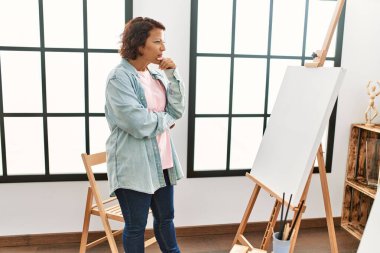 Orta yaşlı İspanyol bir kadın ciddi bir ifadeyle resim stüdyosunda resim çiziyor..