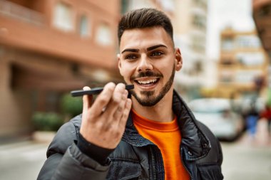 Yakışıklı, sakallı, mutlu ve kendine güvenen, kışlık ceket giymiş telefonda sesli mesaj gönderen bir İspanyol.