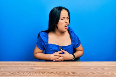 Burnunda piercing olan güzel bir İspanyol kadın elleri karnında masada oturuyor çünkü mide bulantısı, acı verici bir hastalık kendini iyi hissetmiyor. Ağrı kavramı. 