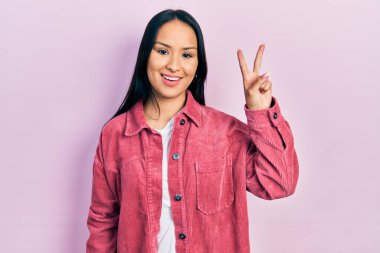 Güzel İspanyol kadın, burun piercingli, sıradan pembe ceketli, iki numaralı parmaklarıyla işaret eden, kendinden emin ve mutlu bir şekilde gülümseyen.. 