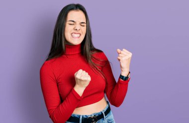 Kırmızı balıkçı yaka kazak giyen genç esmer kız kolları havada ve gözleri kapalı bir şekilde başarıyı kutluyor ve şaşırıyor. Kazanan konsept. 