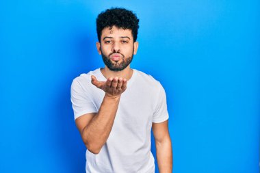 Young arab man with beard wearing casual white t shirt looking at the camera blowing a kiss with hand on air being lovely and sexy. love expression. 