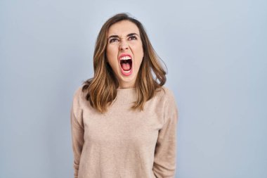 Young woman standing over isolated background angry and mad screaming frustrated and furious, shouting with anger. rage and aggressive concept. 