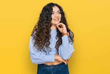 Elleri çenesinde gündelik giysiler içinde soru soran genç İspanyol kız, düşünceli ifade. Gülümseyen ve düşünceli bir yüz. şüphe kavramı. 