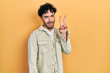 Gündelik kıyafetler giyen, gülümseyen ve kameraya göz kırpan genç İspanyol adam zafer işareti yapıyor. İki numara.. 