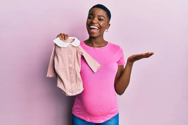 Young African American Woman Expecting Baby Holding Clothes Celebrating Achievement — Fotografia de Stock