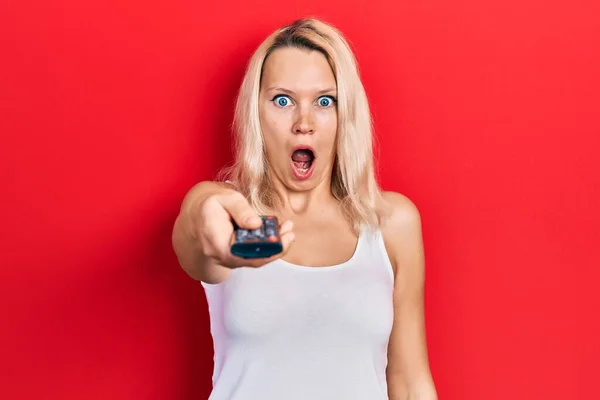 Beautiful Caucasian Blonde Woman Holding Television Remote Control Afraid Shocked — Stockfoto