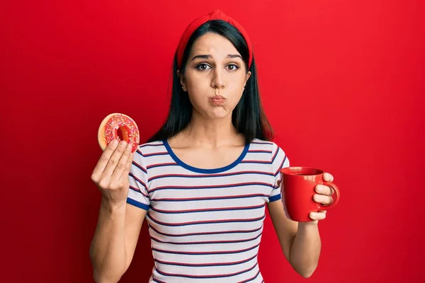 Young Hispanic Woman Eating Doughnut Drinking Coffee Puffing Cheeks Funny — Stock Photo, Image