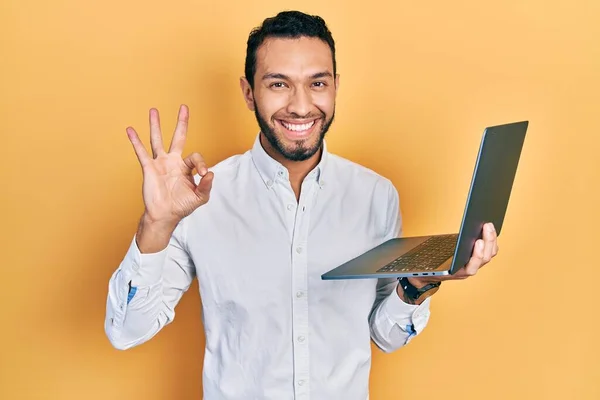 髭を生やしたヒスパニック系の男は 指でOkサインを行うコンピュータのラップトップを使用して作業します 笑顔優しいジェスチャー優れたシンボル — ストック写真