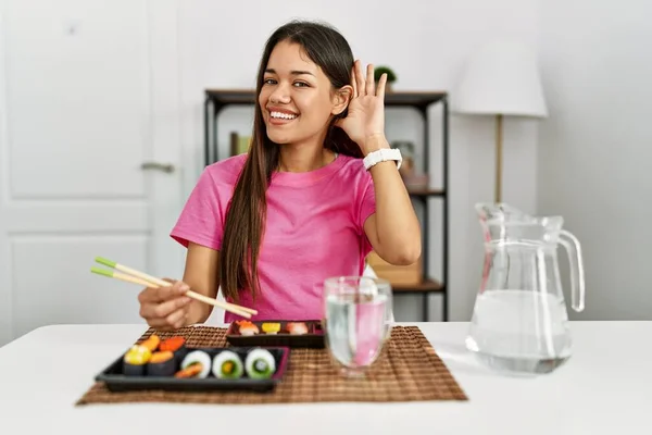 年轻的黑发女人在吃寿司时 用筷子微笑着 两手相对地听着谣言或流言蜚语 聋的概念 — 图库照片