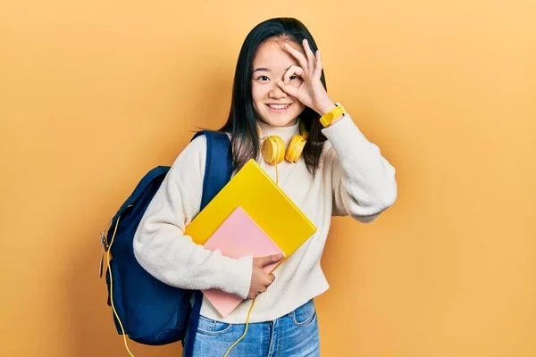年轻的中国女孩拿着学生的背包和书本 手牵着手微笑着做着一个不错的手势 满脸喜色地看着手指 — 图库照片
