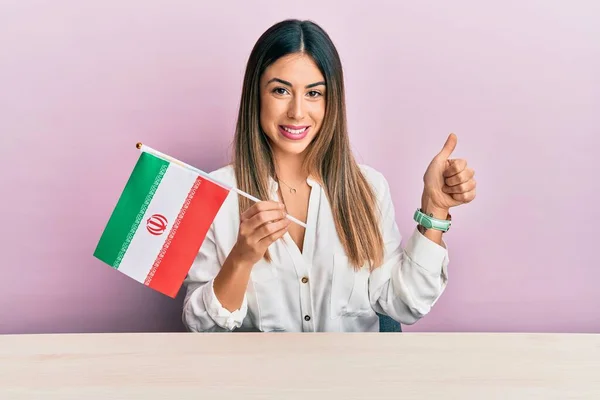 Jovem Hispânica Segurando Bandeira Iran Sentado Mesa Sorrindo Feliz Positivo — Fotografia de Stock