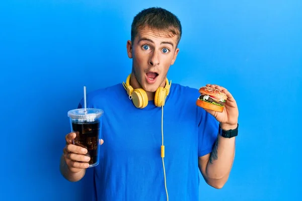 Young Caucasian Man Eating Tasty Classic Burger Soda Celebrating Crazy — стоковое фото