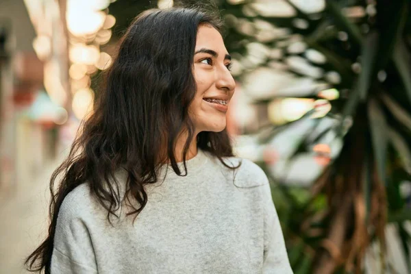 Genç ortadoğulu kız gülümsüyor, mutlu bir şekilde şehirde duruyor..