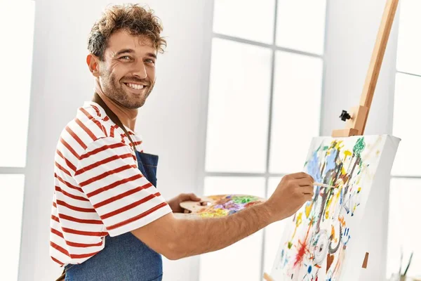 年轻的他惊慌失措的男人带着自信的笑容在艺术工作室里画画 — 图库照片