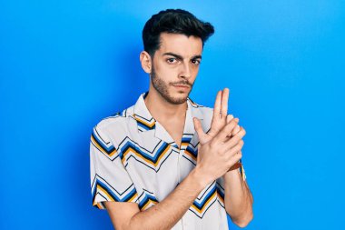 Latin asıllı genç adam gündelik giysiler giyiyor. Elinde sembolik bir silah var. El hareketleriyle cinayet silahlarıyla oynuyor. 