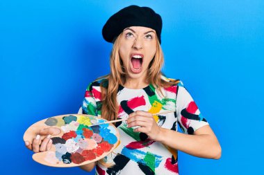 Kafkasyalı genç kadın sanatçı elinde boya fırçası ve palet tutarak kızgın ve kızgın çığlıklar atarak sinirlenmiş ve öfkeliydi. Öfkeyle bağırıyordu.. 