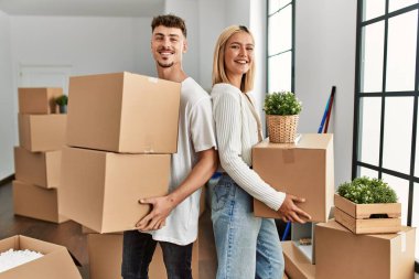 Genç beyaz çift mutlu bir şekilde gülümsüyor. Yeni evlerinde karton kutular tutuyorlar..