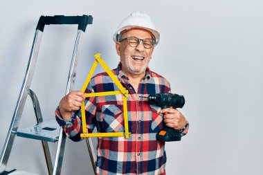 Yakışıklı, elinde tornavida tutan, inşaat merdivenlerinde kasketli, gülen ve kahkahalarla gülen bir adam.. 