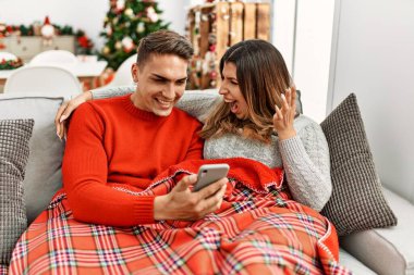 Genç İspanyol çift Noel 'i mutlu bir gülümsemeyle ve ellerini kaldırarak kutlayarak koltukta oturuyor. 