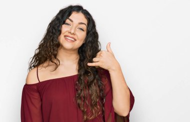 Günlük kıyafetler giymiş, gülümseyen, el ve parmaklarıyla telefon hareketi yapan, telefonda konuşur gibi genç İspanyol bir kız. iletişim kavramları. 