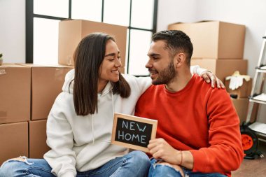 Genç Latin çift gülümsüyor. Yeni ev mesajıyla birlikte ellerinde tahtayla mutlu görünüyorlar..