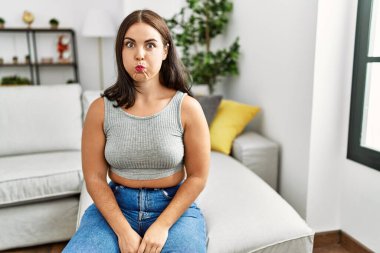 Genç esmer kadın kanepede oturmuş komik suratıyla yanaklarını şişiriyor. Havayla şişmiş ağız, çılgın bir ifade.. 