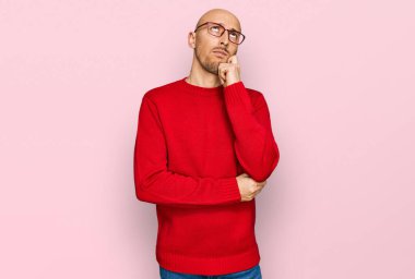 Bald man with beard wearing casual clothes and glasses serious face thinking about question with hand on chin, thoughtful about confusing idea 