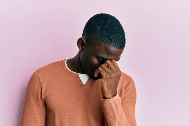 Genç Afro-Amerikan adam günlük kıyafetler giyip yorgun burnu ve gözleri ovuşturup yorgun ve baş ağrısı çekiyor. Stres ve hüsran kavramı. 