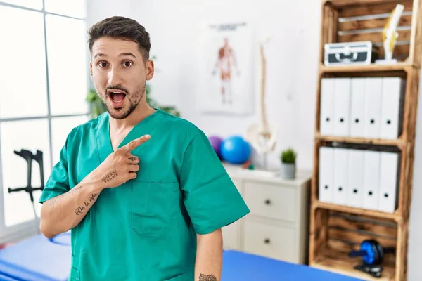 Young Physiotherapist Man Working Pain Recovery Clinic Surprised Pointing Finger — ストック写真