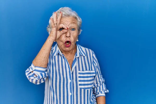 Starsza Kobieta Siwymi Włosami Stojąca Nad Niebieskim Tłem Robiąca Gest — Zdjęcie stockowe