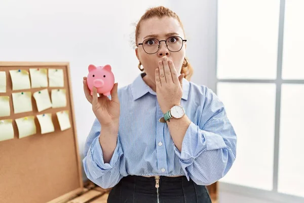 Young Redhead Woman Holding Piggy Bank Office Covering Mouth Hand — Foto Stock