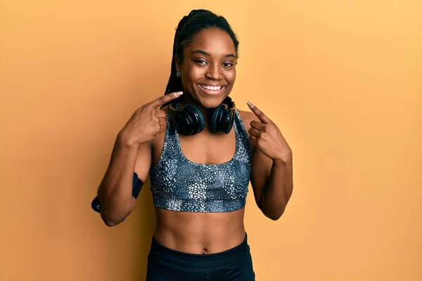 African american woman with braided hair wearing sportswear and arm band smiling cheerful showing and pointing with fingers teeth and mouth. dental health concept.