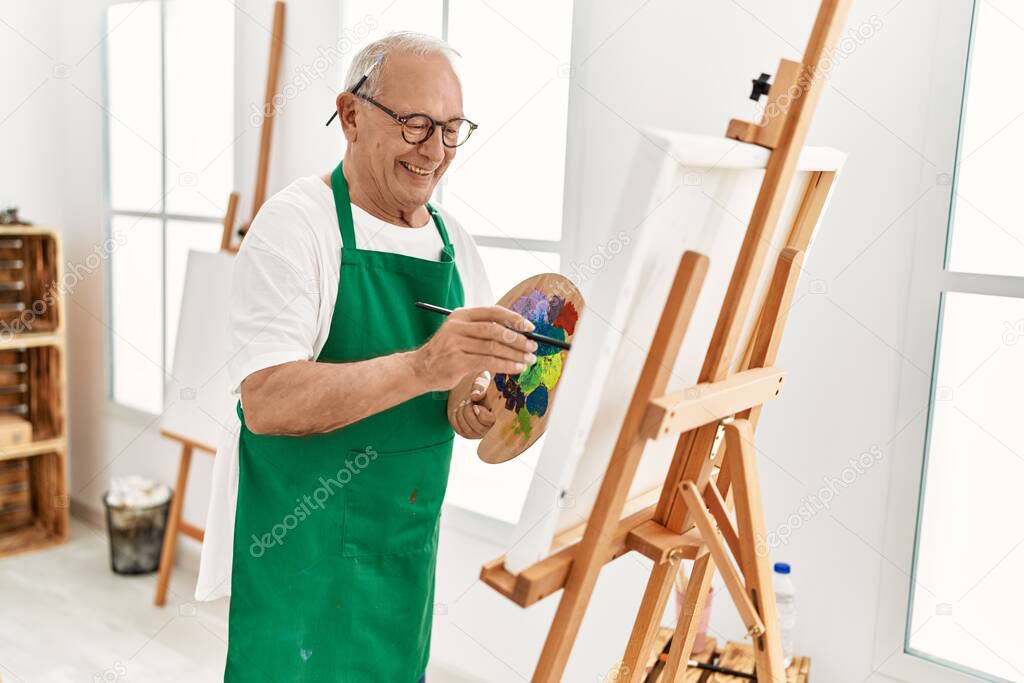 Senior grey-haired artist man smiling happy painting at art studio.