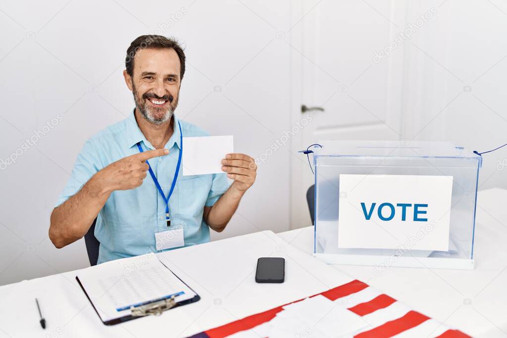 Middle age man with beard voting putting envelop in ballot box smiling happy pointing with hand and finger 
