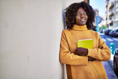 African american woman smiling confident holding book at street